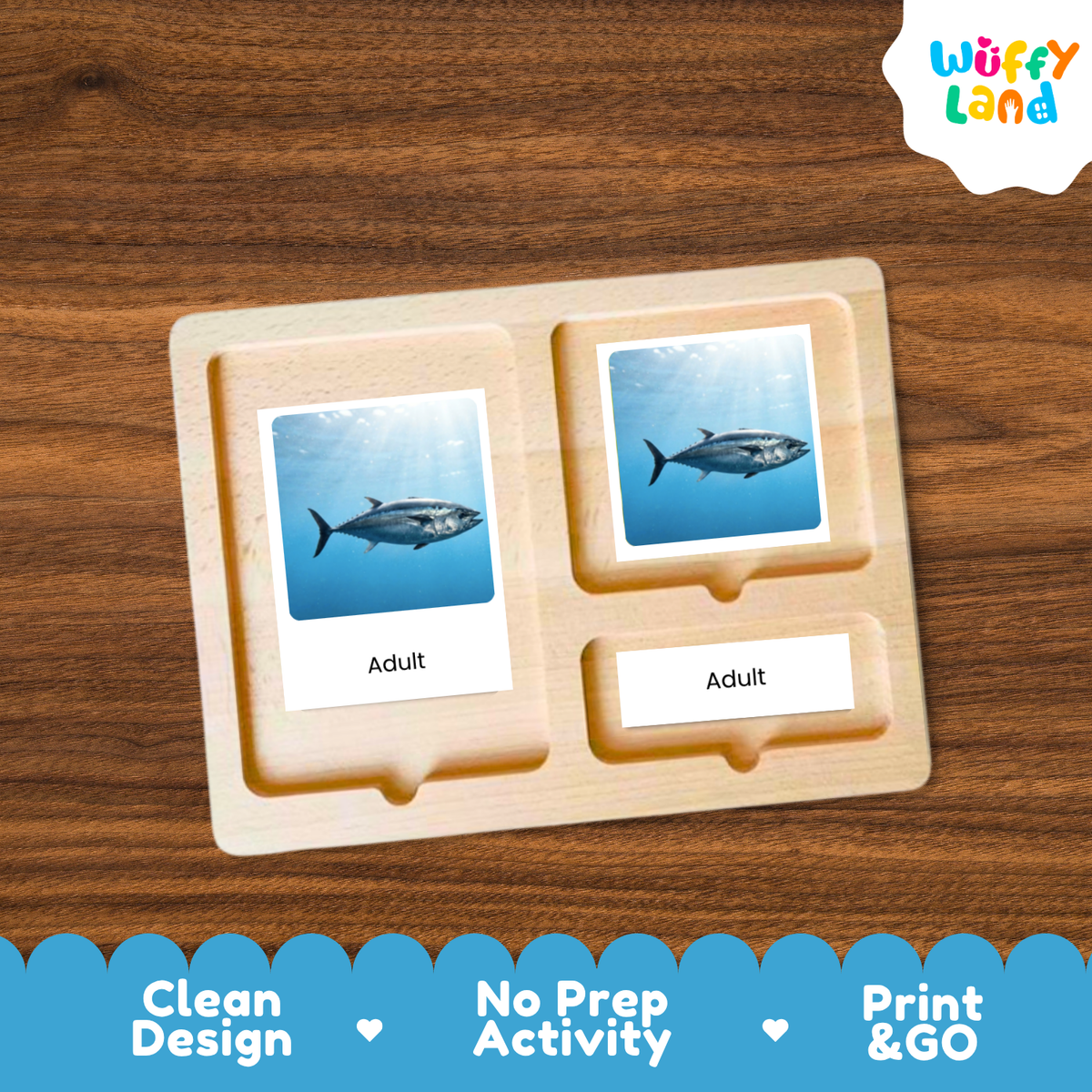 A wooden activity board with two labeled slots reading 'Adult' and pictures of a tuna fish, shown on a wood-grain background. The brand logo 'Wuffy Land' appears in the top right, and marketing text 'Clean Design', 'No Prep Activity', and 'Print & GO' appears along the bottom.