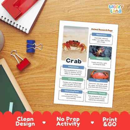 A printed animal research page about a crab is laid on a wooden desk, surrounded by school supplies including a spiral notebook, binder clips, and a red folder. The page has colorful labeled sections and photos of a crab.