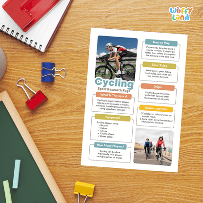 A printed cycling educational poster laid on a wooden desk, surrounded by school supplies including a red notebook, blue and red binder clips, chalk, and paper clips. The poster has colorful text boxes and cycling photos.