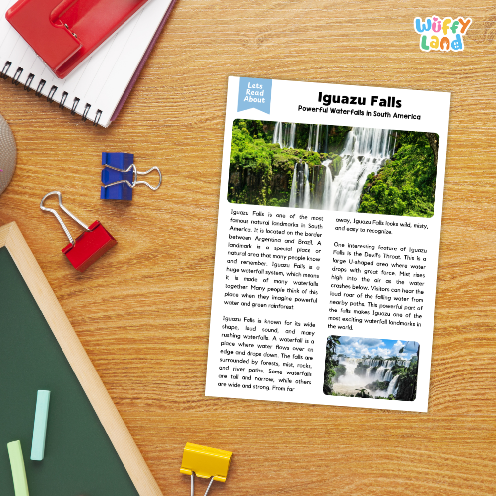 A printed educational poster about Iguguazu Falls laid on a wooden desk, surrounded by school supplies including a red spiral notebook, blue and red binder clips, a green folder, and yellow paper clips. The poster has two photos of the waterfall and the title 'Iguazu Falls' with a 'Let's Read About' header.