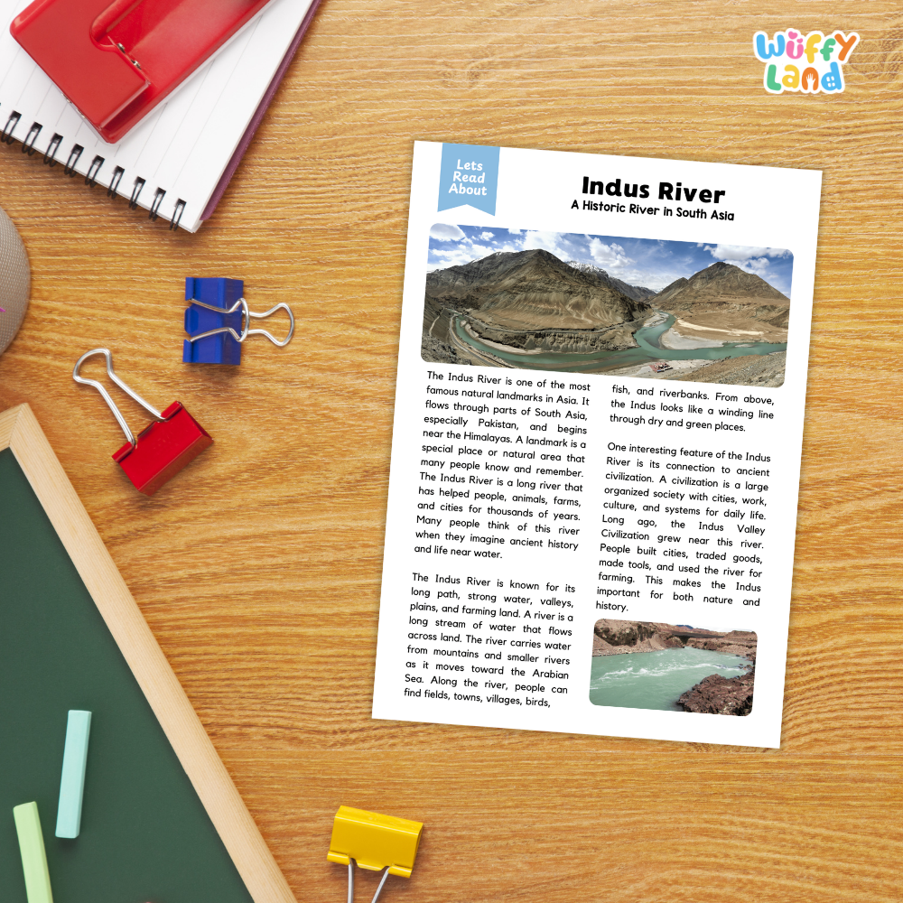 A printed educational poster about the Indus River laid on a wooden desk, surrounded by colorful paperclips, notebooks, and folders.