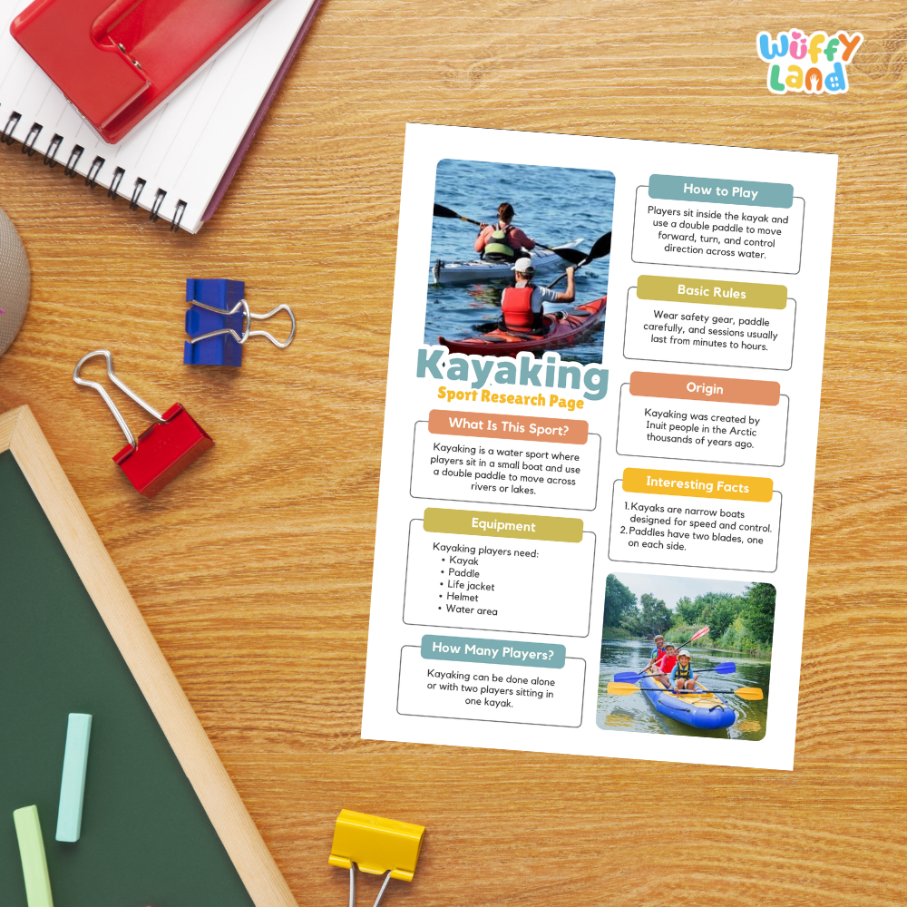 A printed educational poster titled 'Kayaking Sport Research Page' laid on a wooden desk, surrounded by school supplies including a red spiral notebook, blue and red binder clips, a green chalkboard, and yellow and blue chalk.