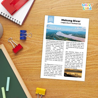 A printed educational poster about the Mekong River lies on a wooden desk, surrounded by school supplies including a spiral notebook, a red notebook, blue and red binder clips, a green folder, and yellow paper clips. The poster has a blue header and includes a small landscape photo of the river.