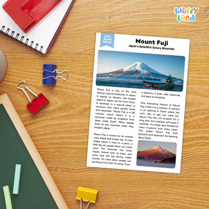 A printed educational worksheet about Mount Fuji titled 'Mount Fuji: Japan's Beautiful Snowy Mountain' laid on a wooden desk, surrounded by colorful paperclips and school supplies. The sheet includes text, a blue header, a mountain photo, and a small Fuji illustration.