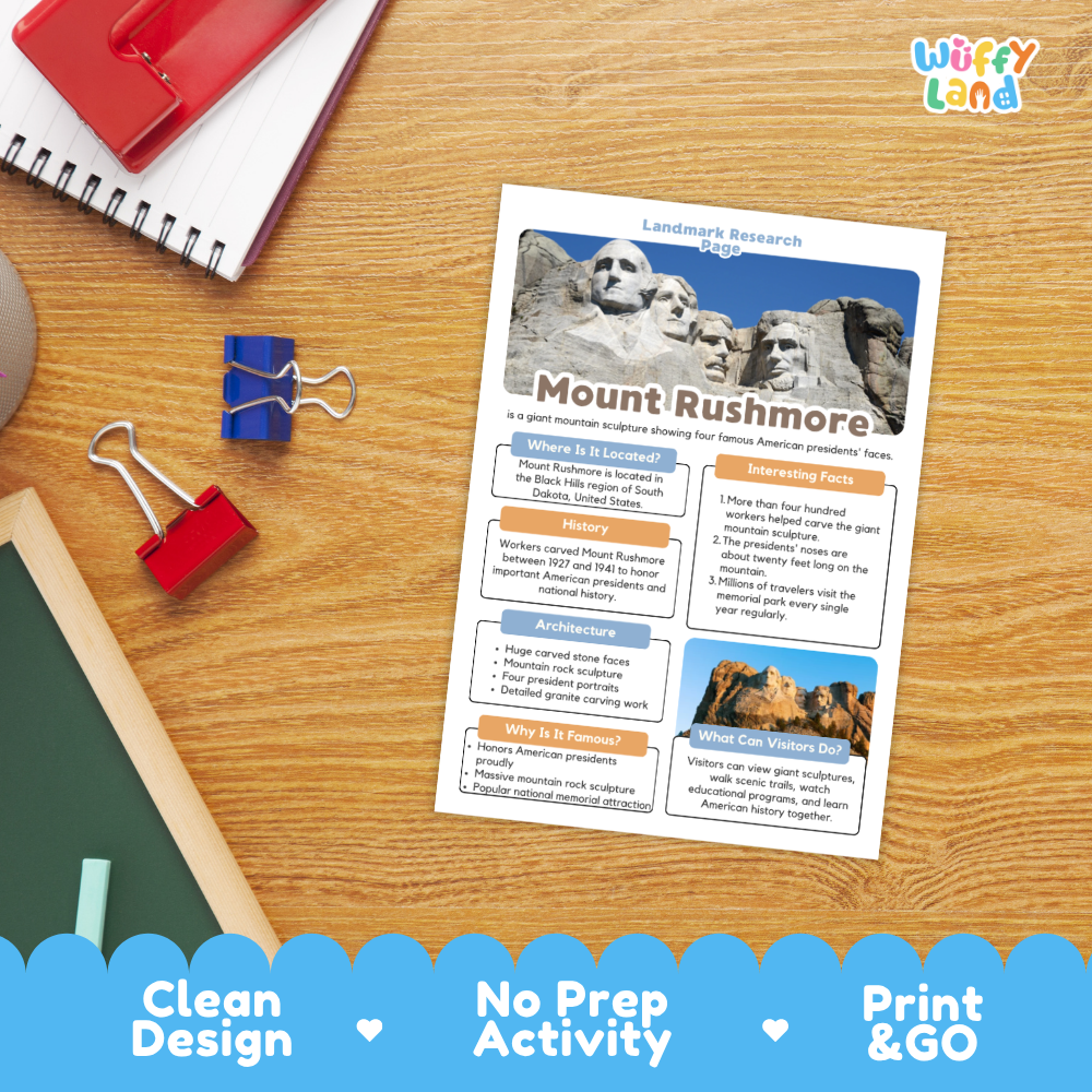 A printed Mount Rushmore landscape research guide sheet laid on a wooden desk, surrounded by school supplies including a red notebook, binder clips, and a chalkboard. The sheet has colorful text blocks and a large mountain landscape photo at the top.