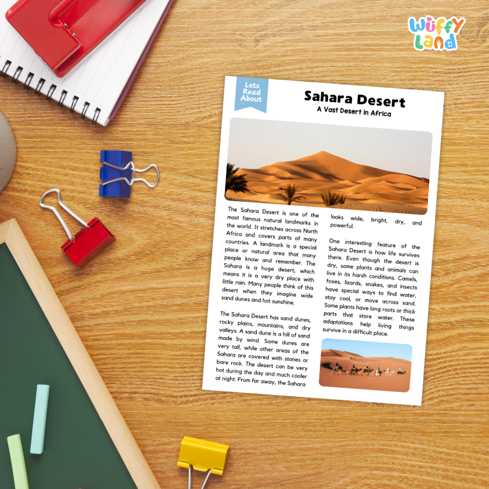A children's educational worksheet titled 'Sahara Desert: A Visit Desert in Africa' from the brand 'Wiffly Land' is displayed on a wooden desk alongside colorful school supplies like a red spiral notebook, blue and red binder clips, a green folder, and a yellow paperclip.