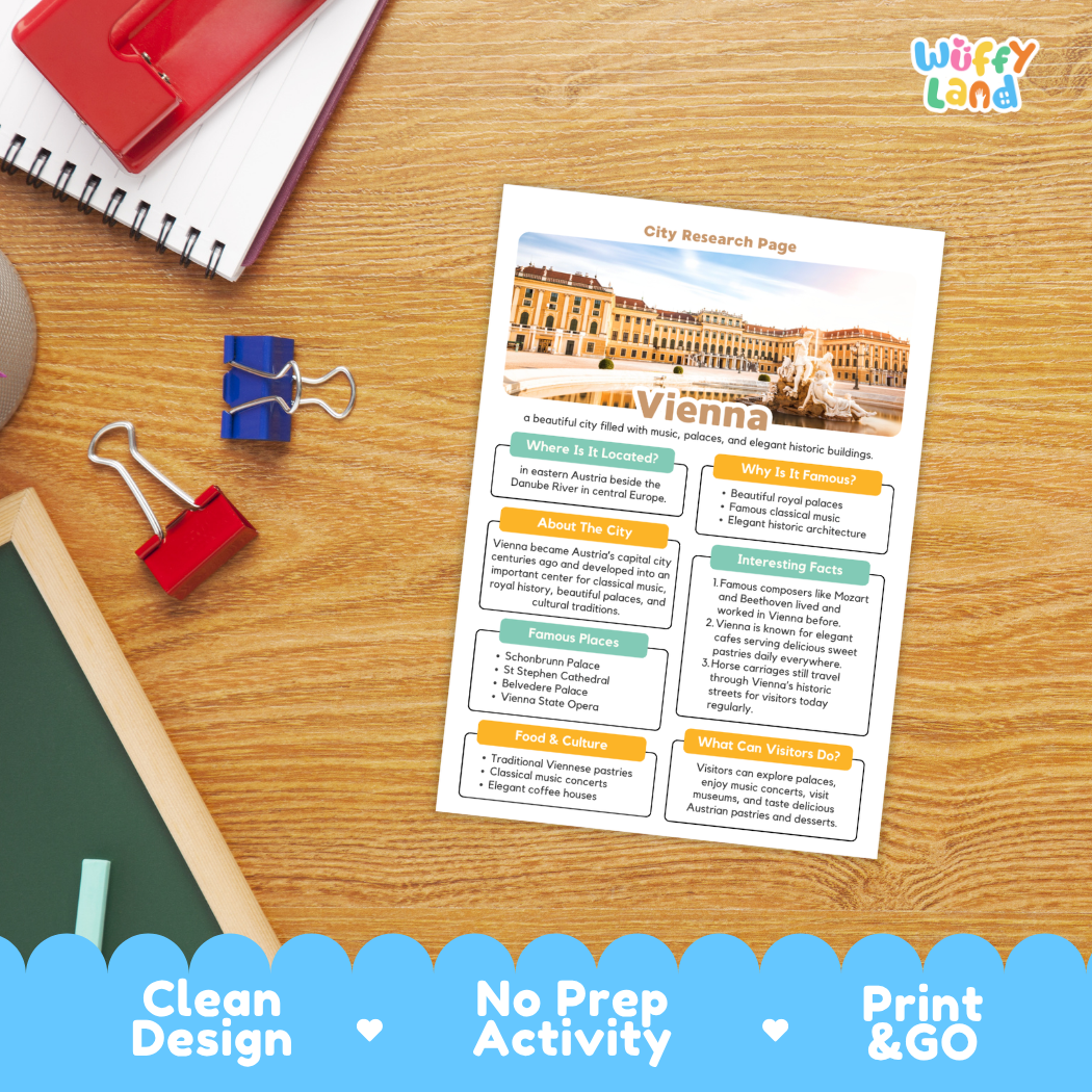 A printed city research page about Vienna is shown on a wooden desk with school supplies around it. The page has a white background with colorful text boxes, a building photo, and headings including 'City Research Page' and 'Vienna.