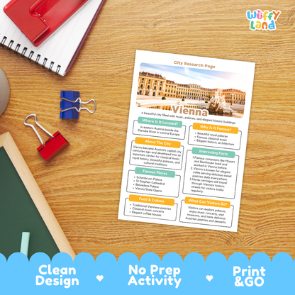 A printed city research page about Vienna is shown on a wooden desk with school supplies around it. The page has a white background with colorful text boxes, a building photo, and headings including 'City Research Page' and 'Vienna.
