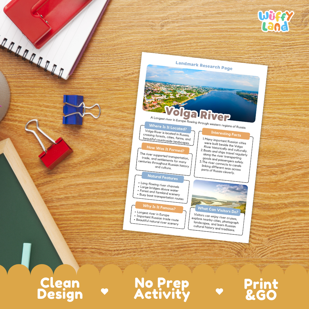 A printed educational worksheet titled 'Volga River' laid on a wooden desk, surrounded by school supplies including a spiral notebook, a red notebook, binder clips, and a chalkboard. The sheet has a clean design with a river landscape photo at the top and text boxes below.