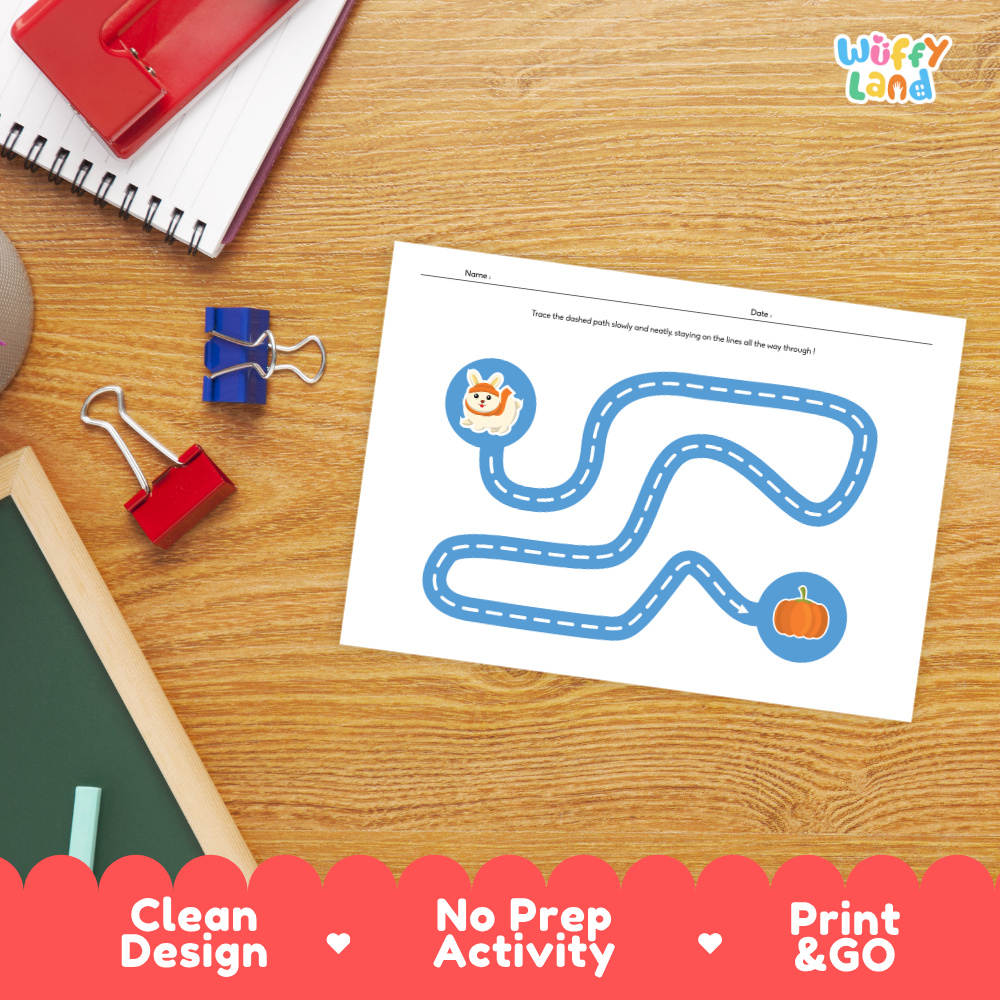 A children's printable activity sheet on a wooden desk, featuring a blue dashed path with a cat at one end and a pumpkin at the other. The sheet is surrounded by school supplies, including a spiral notebook, binder clips, and a chalkboard edge.