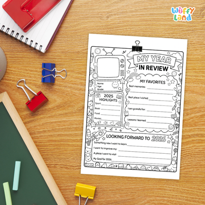 A black-and-white printable planner page titled 'MY YEAR IN REVIEW' laid on a wooden desk, surrounded by school supplies including a spiral notebook, binder clips, chalk, and a green board. The logo 'wiffy land' appears in the top right corner.